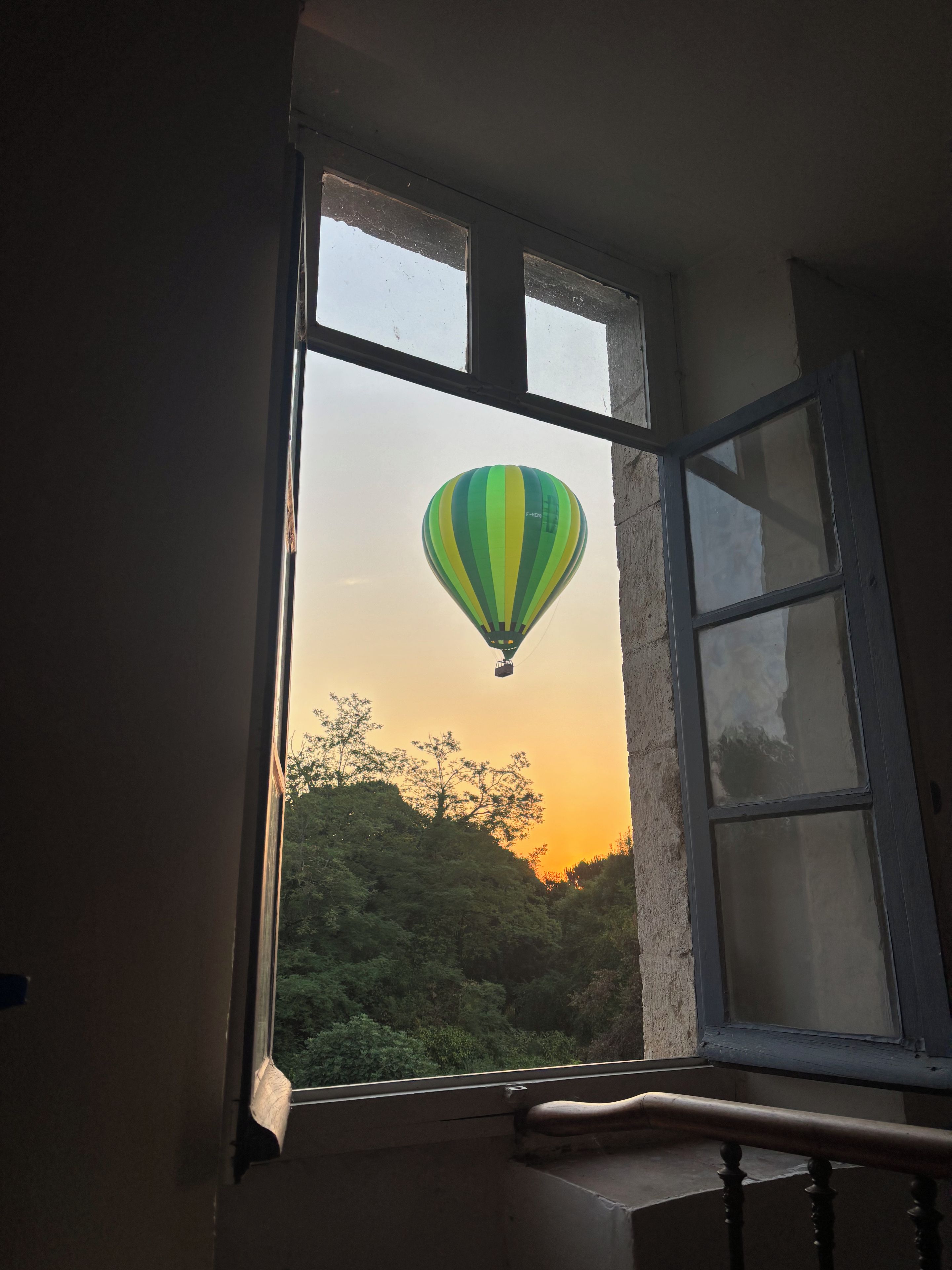 A window with a view of a green and yellow hot air balloon against a sunset sky.
