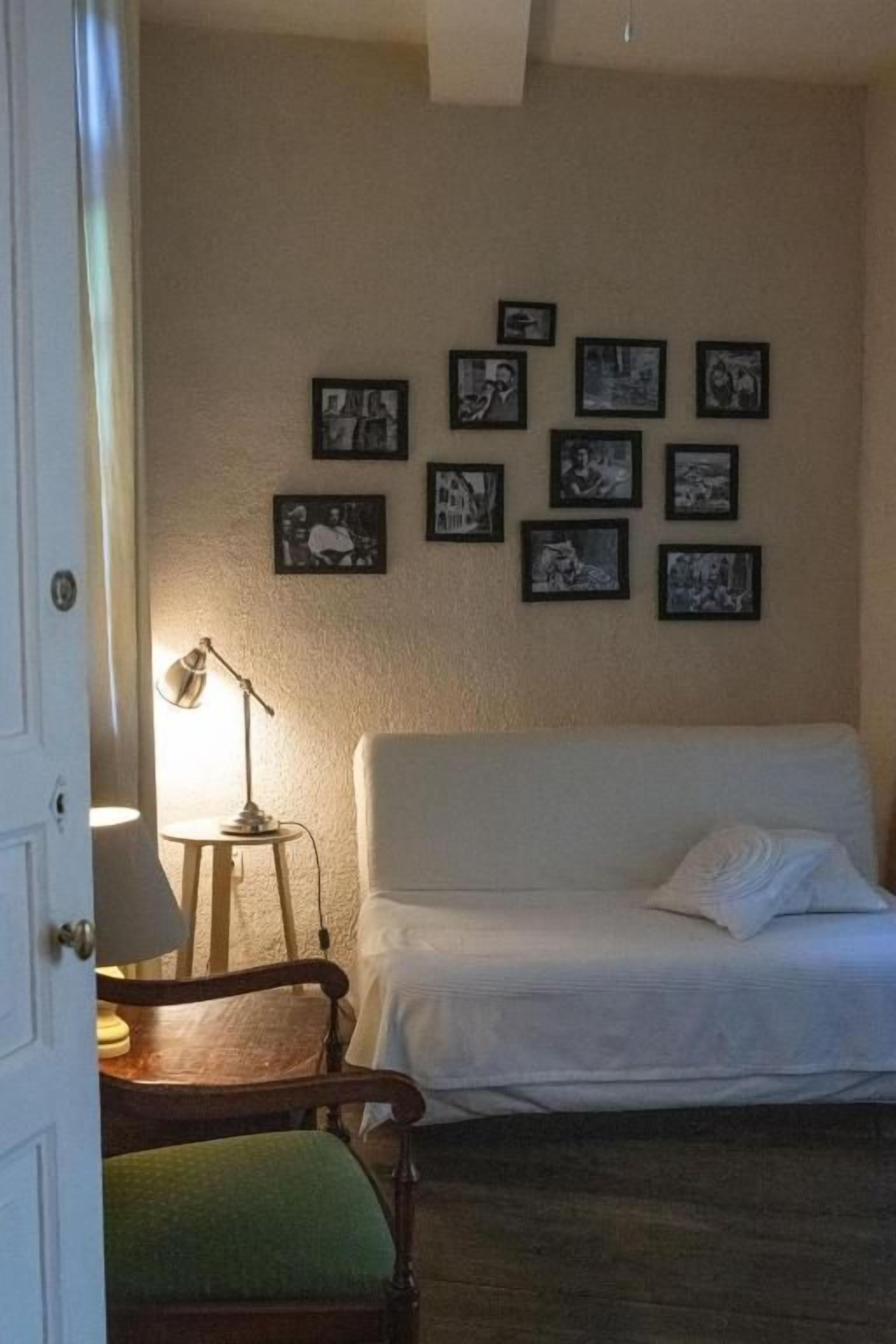 Un dormitorio con cama, una silla, un escritorio y una pared decorada con cuadros.