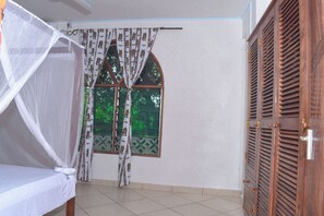 A room with a bed, a window with patterned curtains, and a wooden door. - 3-Bedroom Apartment with AC in Mtwapa (Mtwapa)