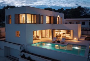 Ein modernes, zweistöckiges Haus mit Pool, Essbereich und Wohnzimmer mit Kamin.
