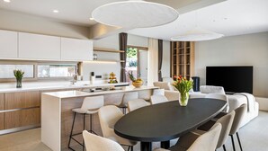 Una cucina moderna con isola centrale, sgabelli da bar, tavolo da pranzo e televisione a schermo piatto.
