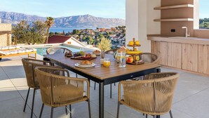 Zona pranzo con vista su una cittadina costiera, piscina e cucina esterna.