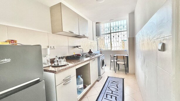 Una cocina compacta con refrigerador, estufa, lavamanos y un pequeño comedor con sillas.