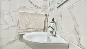 Un baño con un lavamanos blanco, una toalla colgada en un perchero y una botella de jabón en la encimera.