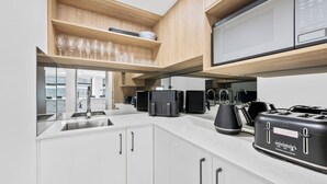 Une cuisine moderne avec des meubles blancs, un évier en acier inoxydable et un grille-pain noir.