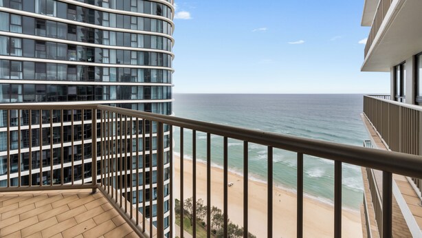 Un bâtiment moderne à la façade incurvée, doté d’un balcon avec une rambarde en métal, et offrant une vue sur la plage et l’océan.
