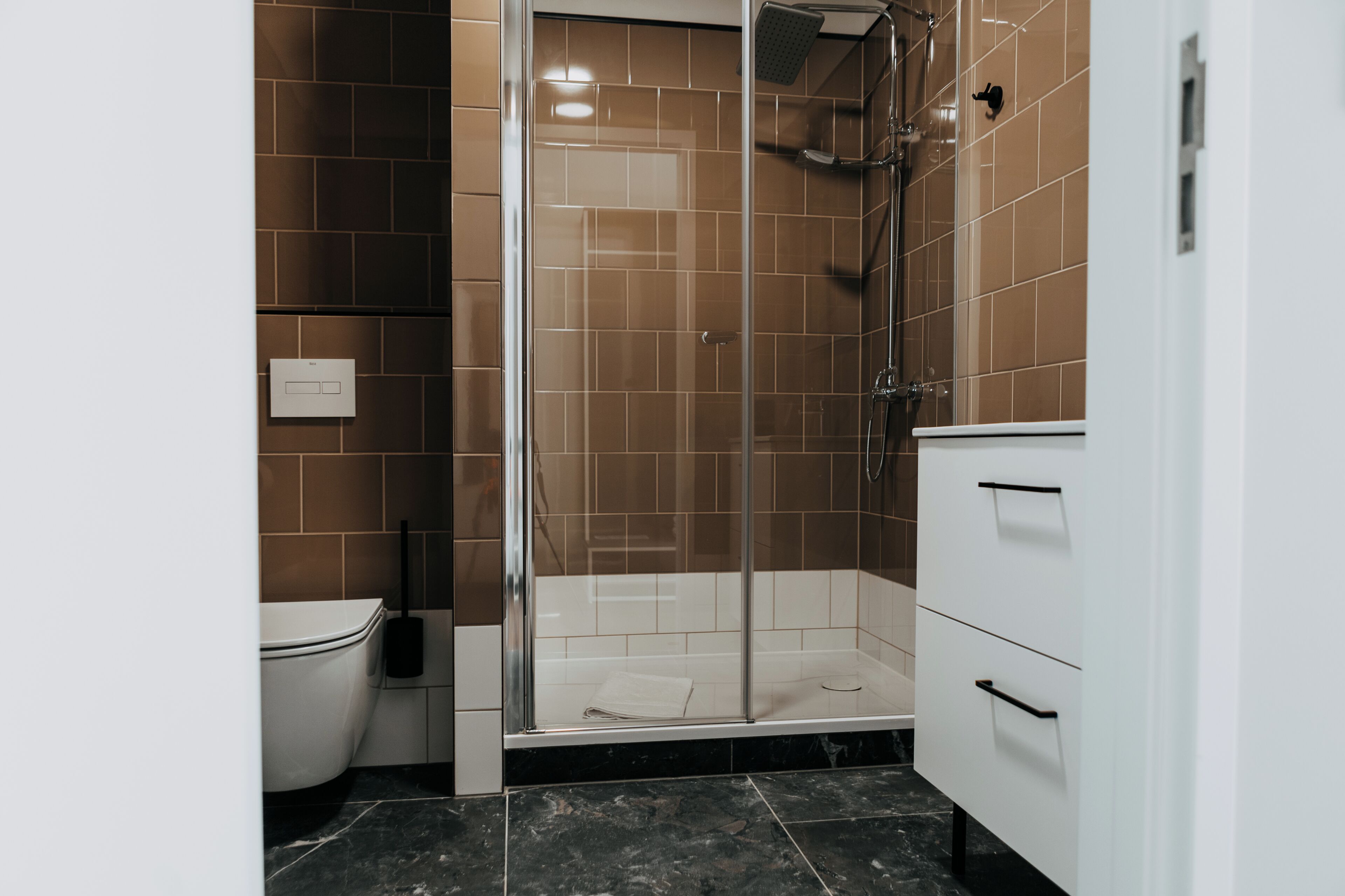Een badkamer met douche, toilet en witte badkamerkastjes.