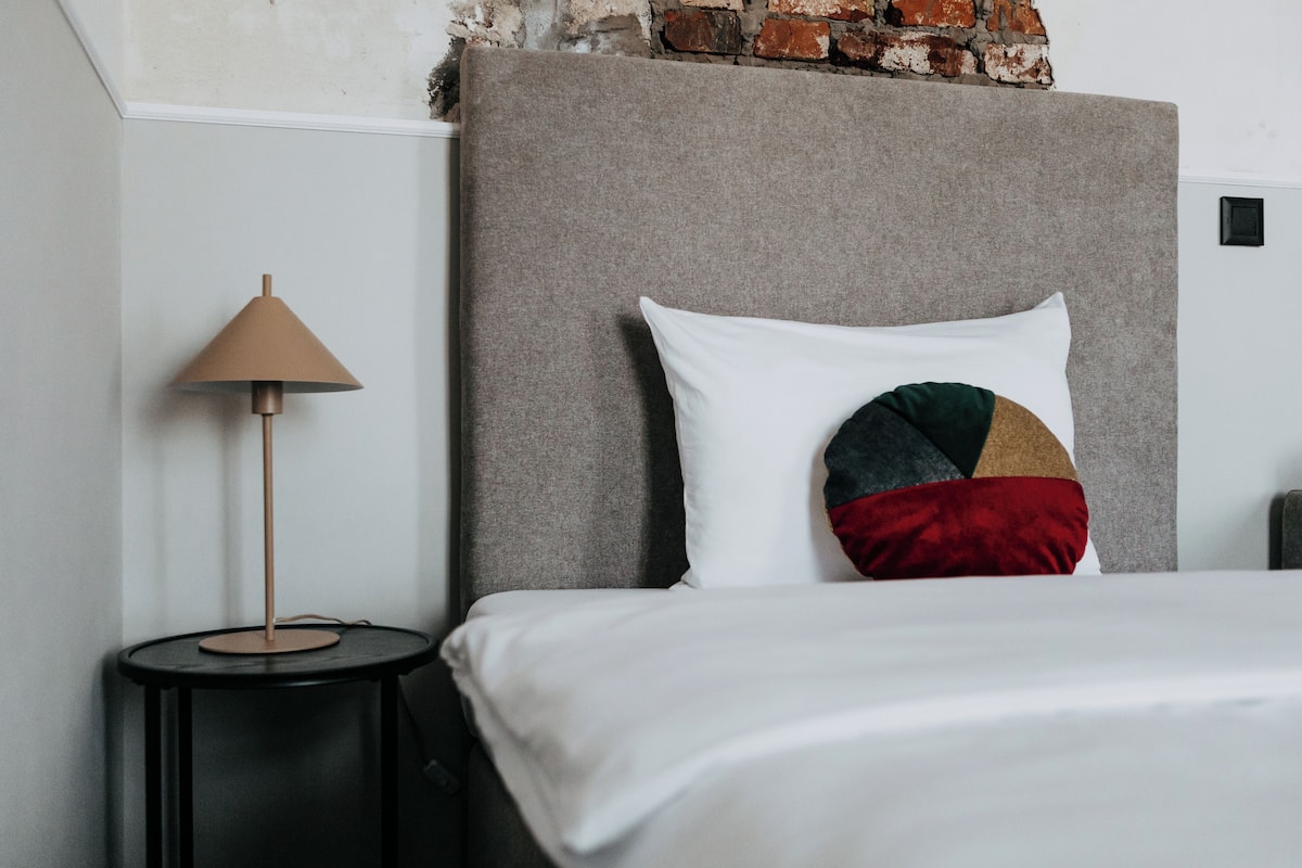A bed with a grey headboard, a white pillow, and a multi-colored pillow.