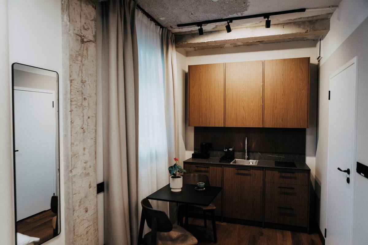 A compact kitchen with wooden cabinets, a black countertop, and a small dining table with a chair.