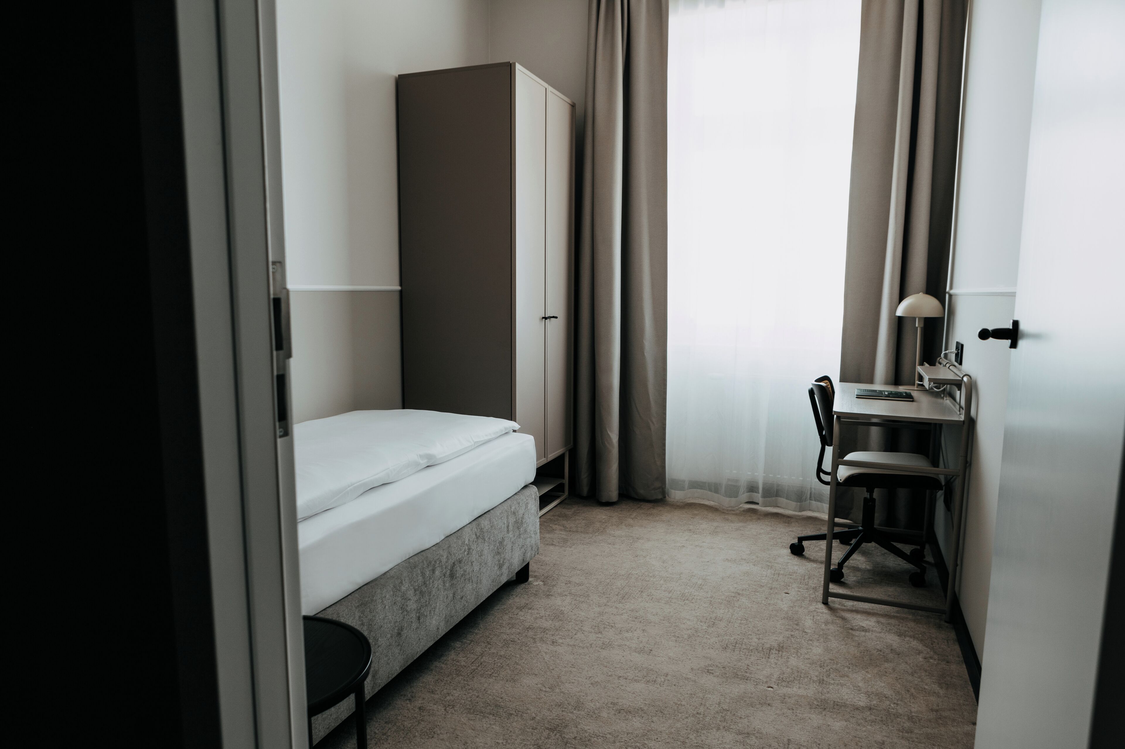 Een kleine, praktische kamer met een bed, een bureau en een stoel.
