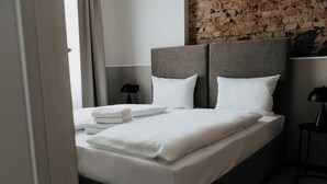 A neatly made bed with white linens and pillows, a headboard, and a lamp on a bedside table.