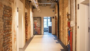 A corridor with exposed brick walls, white tiled floors, and visible HVAC ducts.