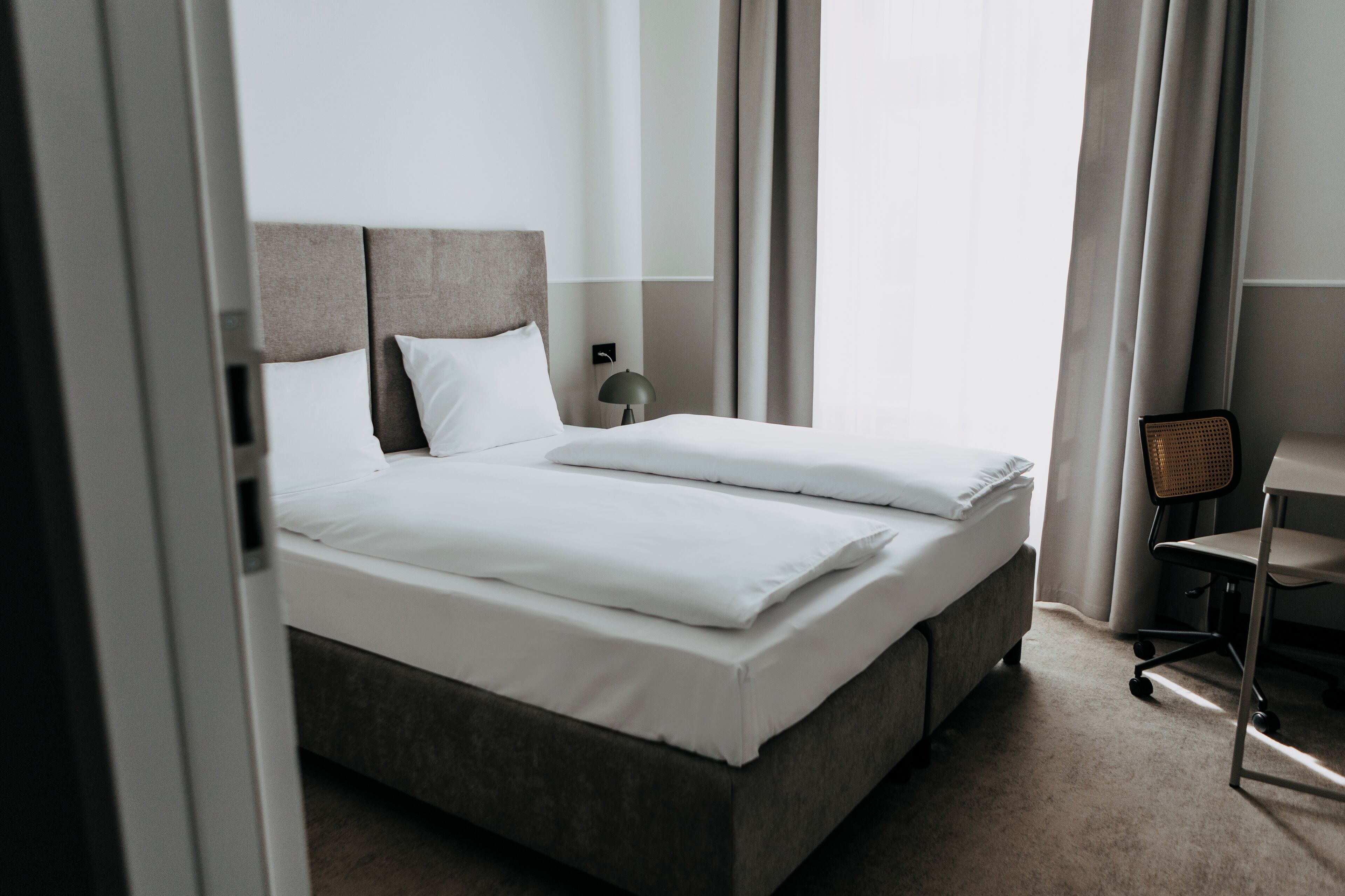 A hotel room with a bed, a chair, a desk, and a lamp.