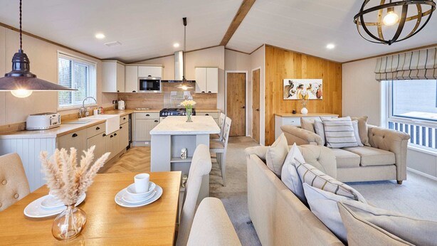 Eine moderne Küche mit weißen Schränken, einer zentralen Kochinsel und einem Essbereich mit Holztisch und beigefarbenen Sofas.