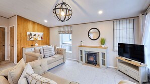 Ein Wohnzimmer mit beiger Sofagarnitur, Kamin, Fernseher und einer Wand im Holzoptik.