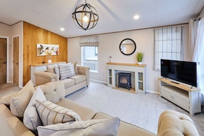 A living room with a beige sofa set, a fireplace, a TV, and a wooden accent wall. - Host Stay Huckleberry Lodge (York)