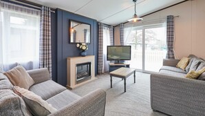 Ein Wohnzimmer mit Kamin, Sofa, Fernseher und Blick ins Freie.