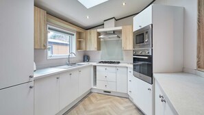 Eine moderne Küche mit weißen Schränken, einem Gasherd, einer Mikrowelle und einem Fenster mit Jalousien.