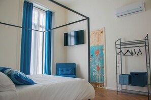 Ein Schlafzimmer mit einem Bett, einem Sessel, einem Fernseher, einer Klimaanlage und einer Wand mit einem Regal.