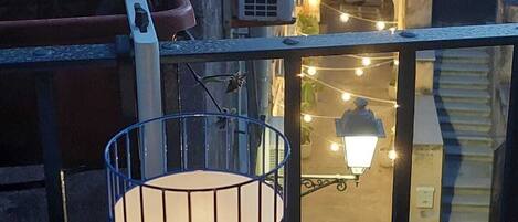 A balcony with a metal railing, a potted plant, and a white lamp.