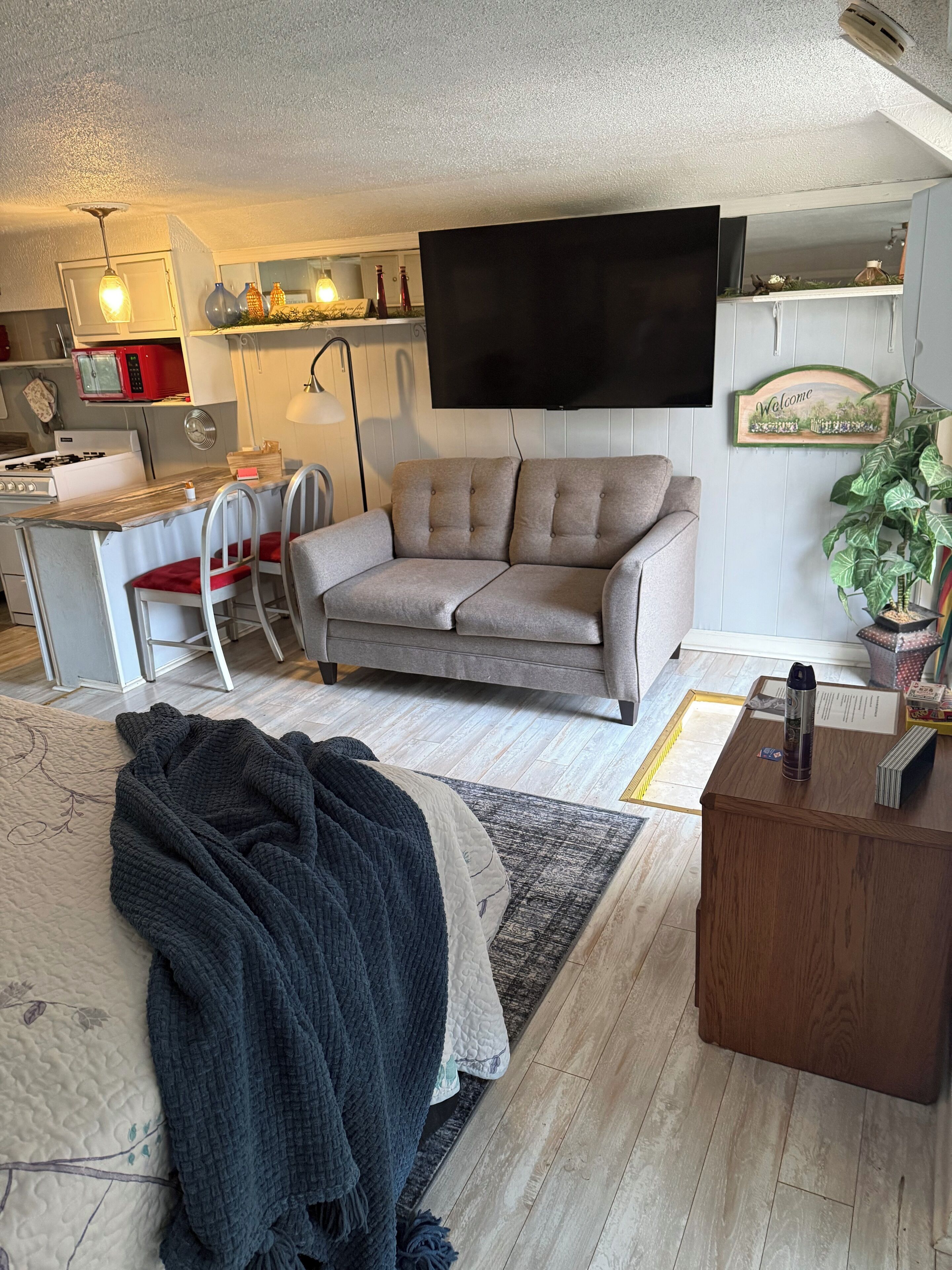 Un espacio habitable compacto con sofá, una mesa de centro, televisor montado en la pared, zona de cocina con microondas y mesa de comedor con sillas.
