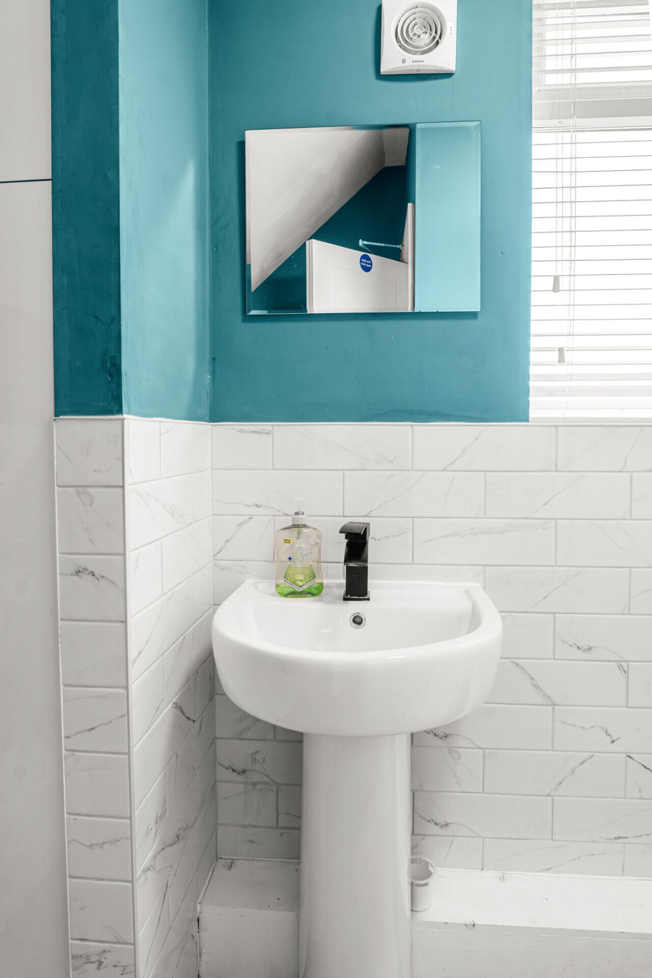 Une salle de bain avec un lavabo blanc, un miroir et un mur bleu.