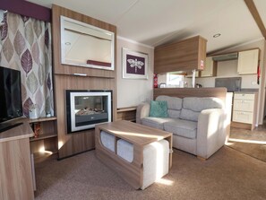 Indretning i en kompakt autocamper med sofa, tv, pejs og et tekøkken.