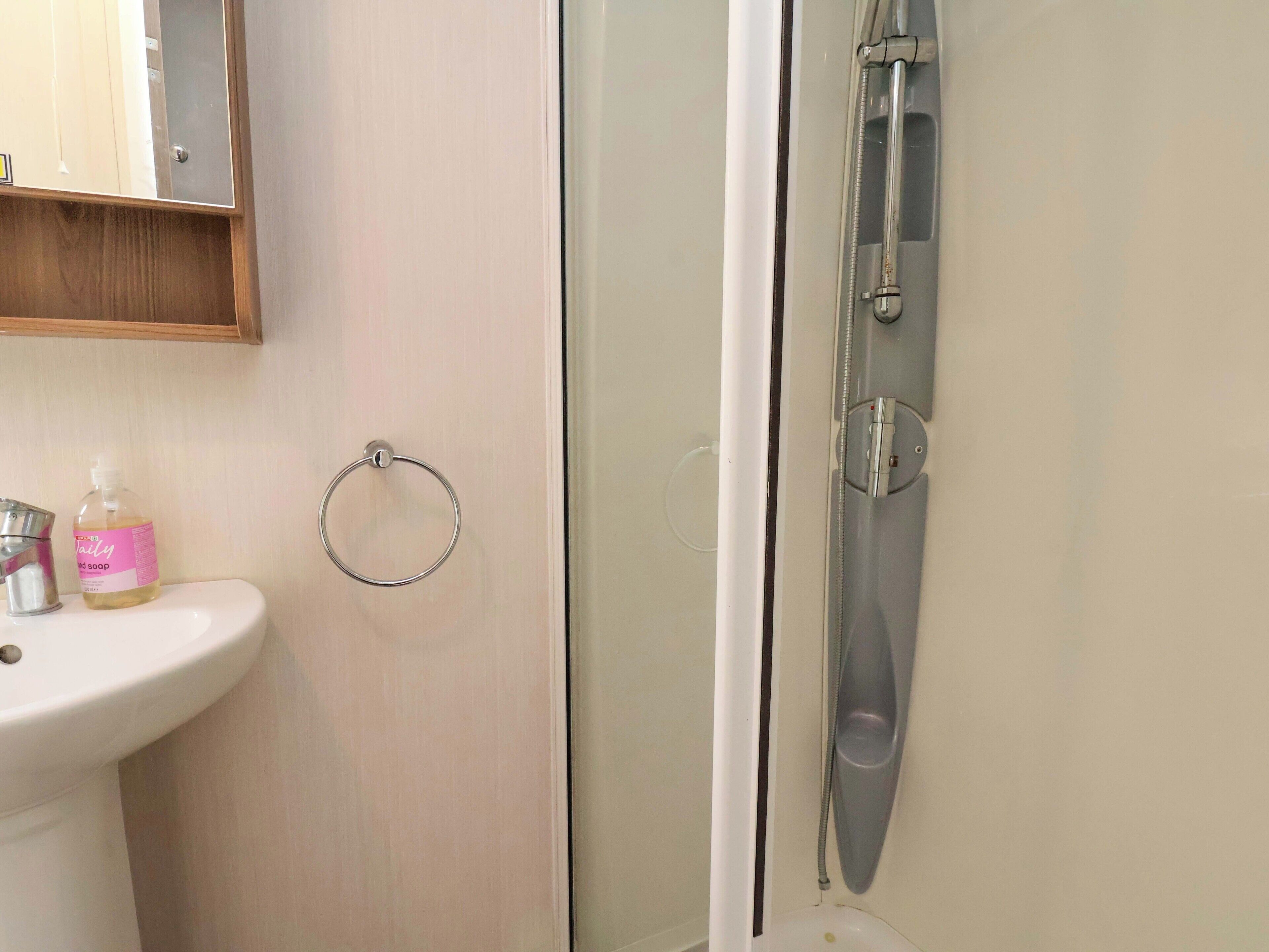 Casa de banho com lavatório, dispensador de sabonete líquido, suporte para toalha e cabine de duche.