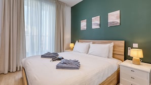 Uma cama bem arrumada com almofadas e toalhas, um abajur e uma obra de arte na parede.