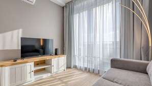 Sala moderna com televisão de tela plana em um console de madeira, sofá cinza e cortinas leves.