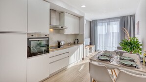 Cozinha moderna com eletrodomésticos embutidos, área de jantar com mesa posta para quatro pessoas e uma janela grande com cortinas.
