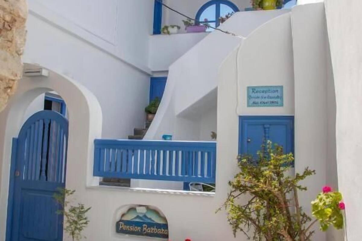 A narrow street with white buildings, blue doors, and potted plants.