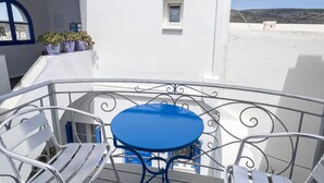 Un balcon avec une table et des chaises, une petite fenêtre et des plantes en pot.