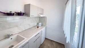 Une cuisine moderne avec des meubles blancs, un plan de travail en marbre et une fenêtre agrémentée de rideaux blancs.