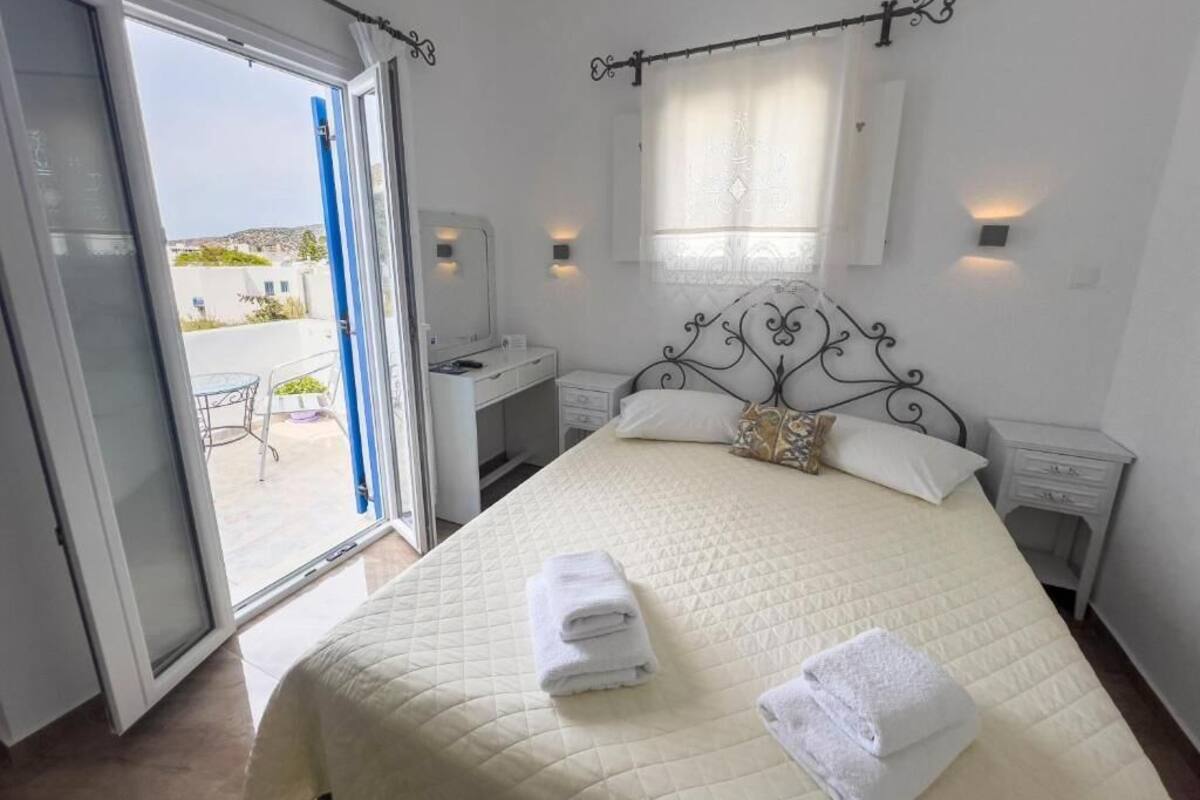 A bedroom with a bed, a desk, and a chair. There is a window with curtains and a view of the outside.