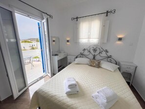 Ein Schlafzimmer mit Bett, Schreibtisch und Stuhl. Ein Fenster mit Vorhängen bietet einen Blick ins Freie.