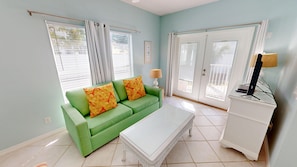 A living room with a green sofa, two pillows, a white coffee table, and a TV on a white cabinet. - Toes In The Sand 4 Bedroom Home (Destin)