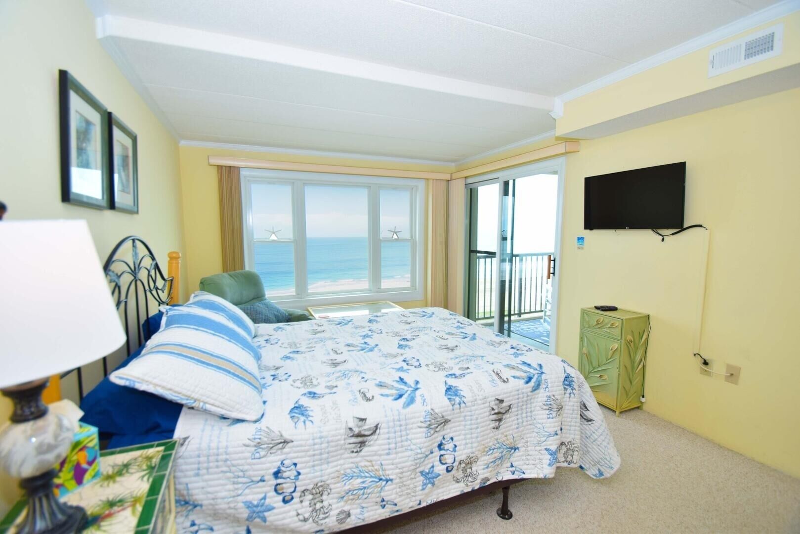 Una camera da letto con un letto, una sedia, una TV, una finestra vista mare e un balcone.