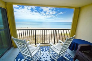 A balcony with a view of the beach, white chairs, and a blue table. - Sandpiper Dunes 605 2 Bedroom Condo (Ocean City)