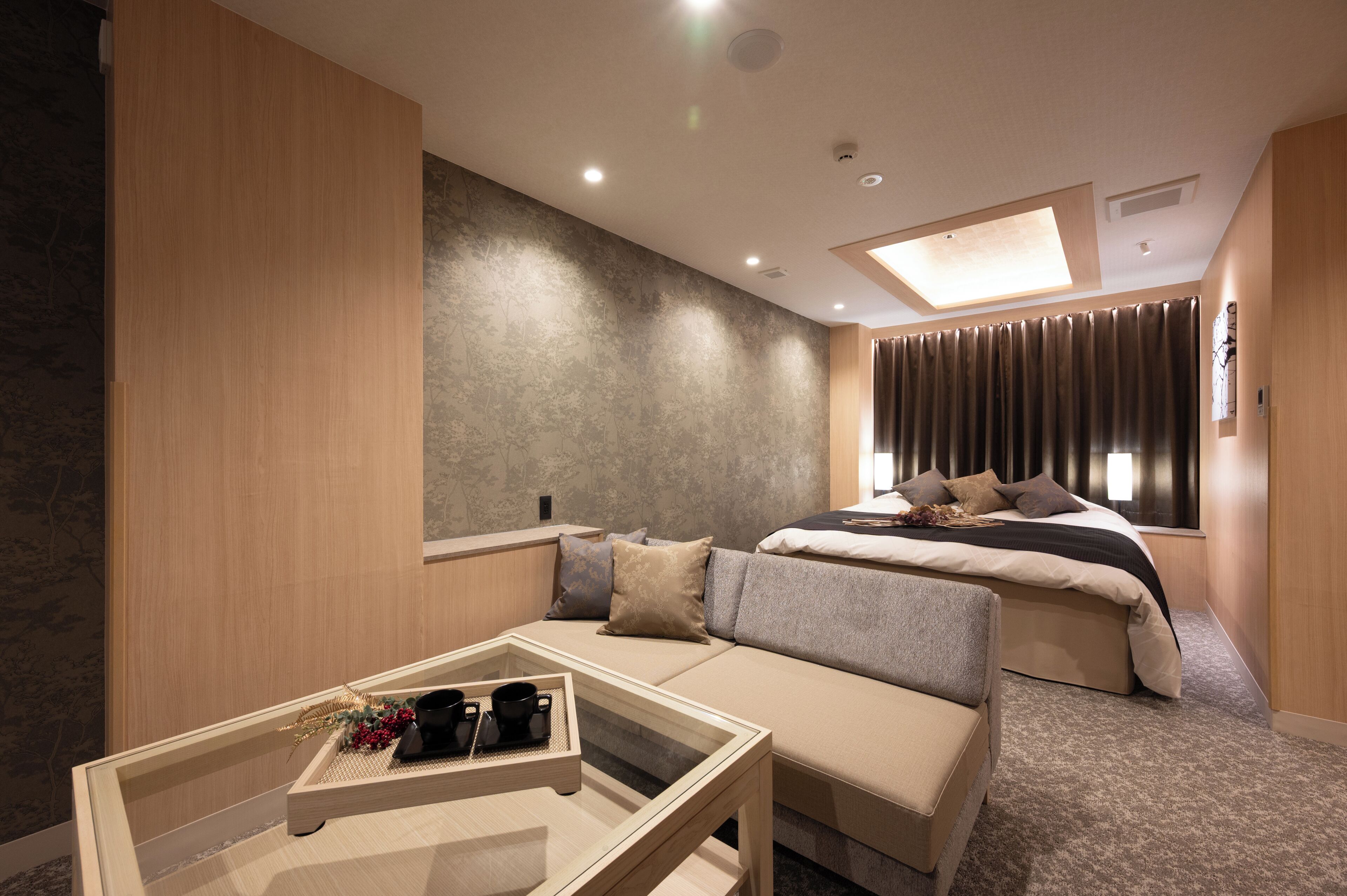 A modern hotel room with a sofa, a bed, a small table with a tray, and a window with curtains.