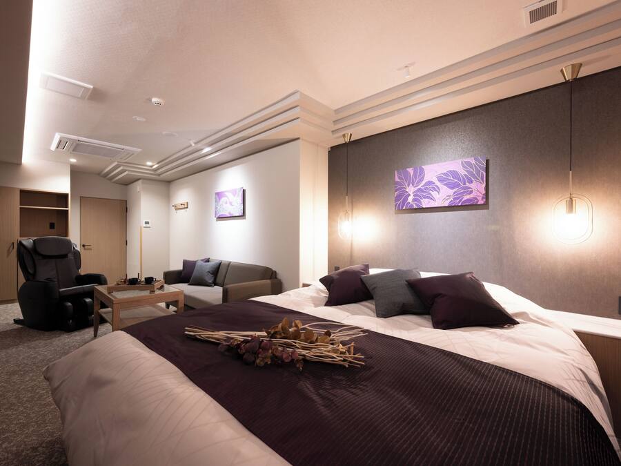 A hotel room with a large bed, a desk, a chair, and a sofa.