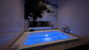 A modern bathroom with a large bathtub, a wall-mounted mirror, and a black abstract painting. - HOTEL ZEN narahourai (Nara)