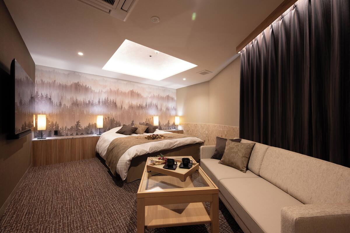 Una habitación de hotel con cama, sofá, mesa de centro y un mural en la pared.