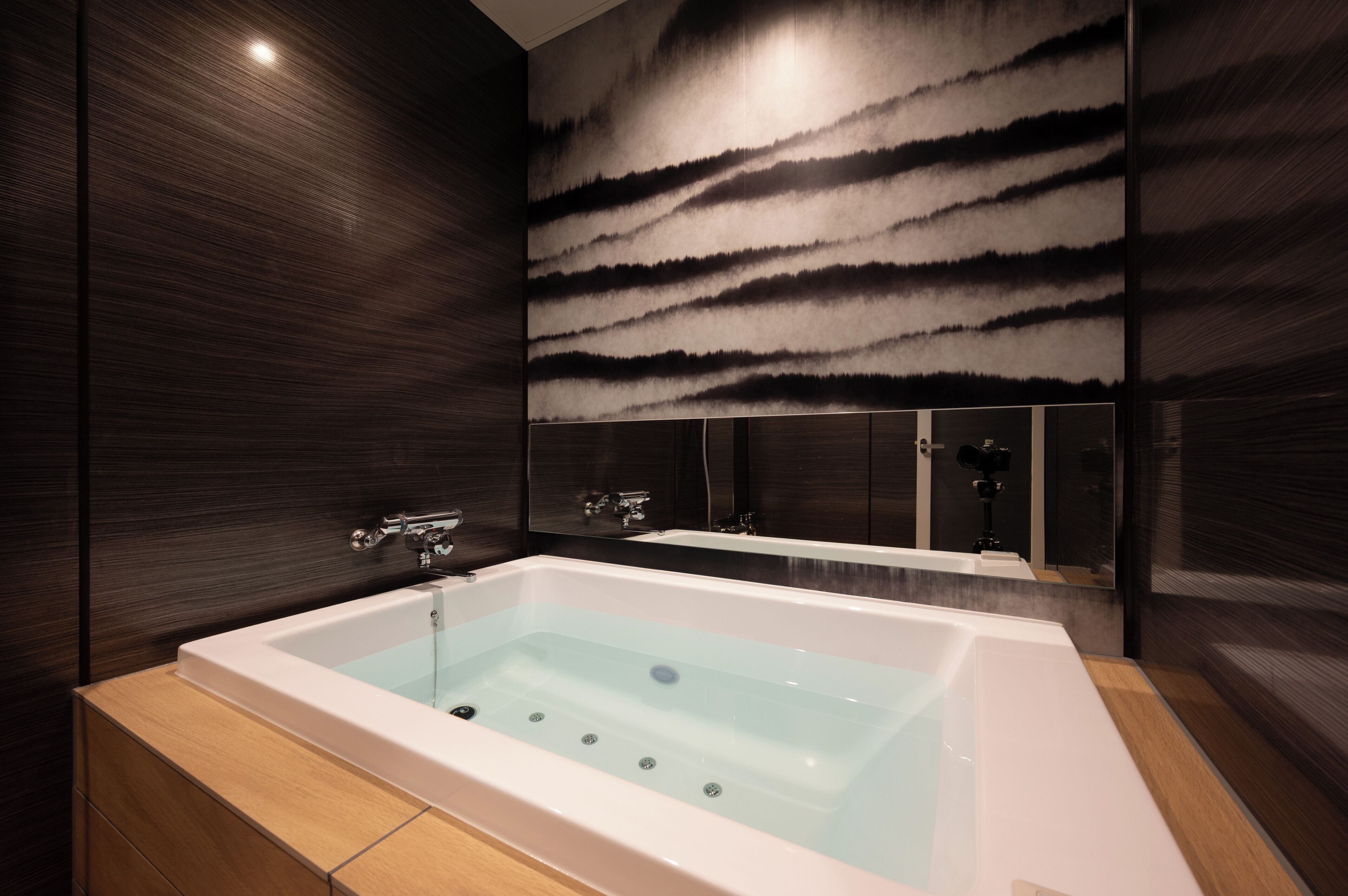 Ein modernes Badezimmer mit einer großzügigen Badewanne, dunklen Holzwänden und einem spiegelnden Spiegel.