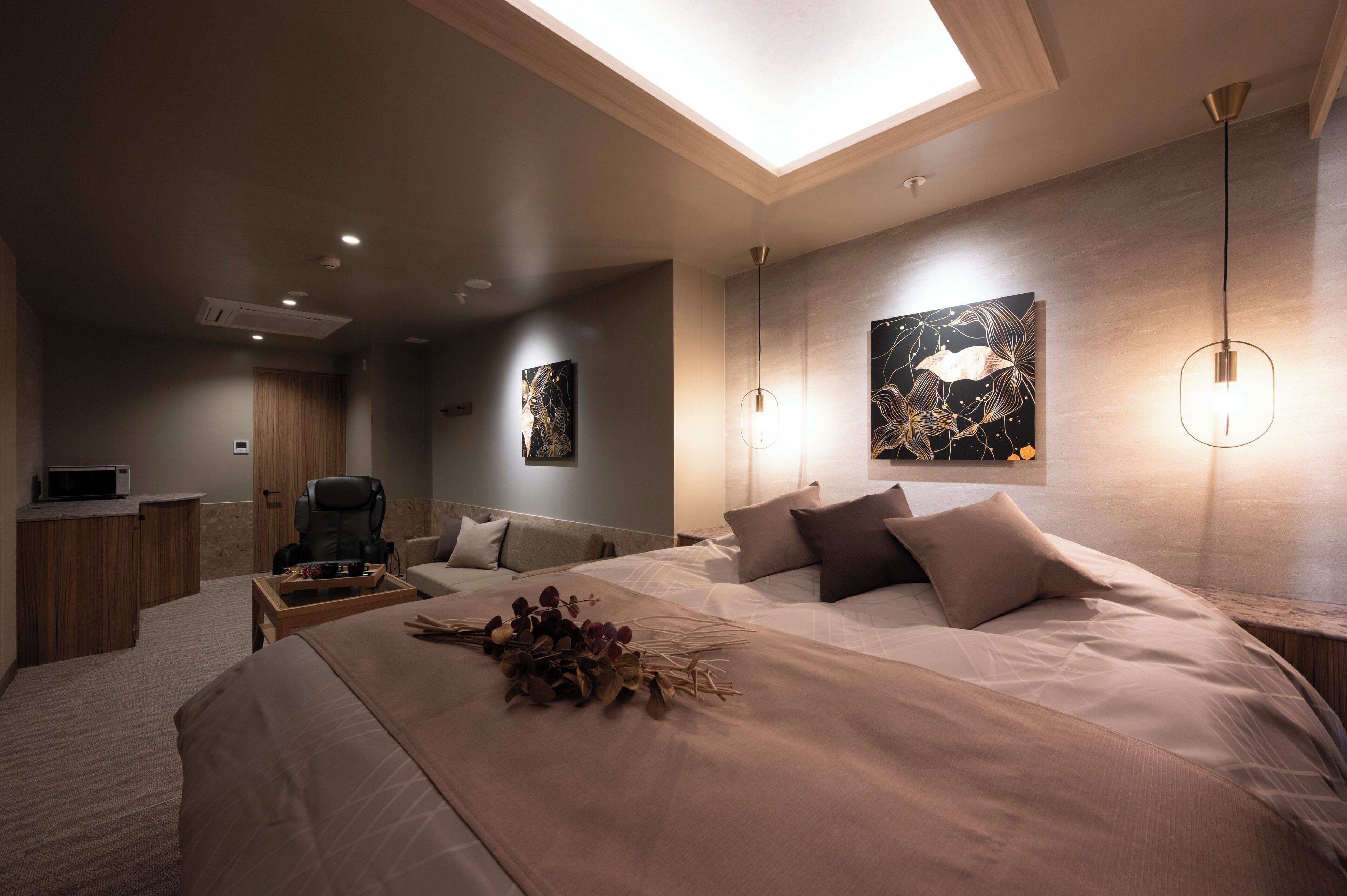A modern bedroom with a skylight, a bed with a decorative arrangement, a desk, and artwork on the walls.