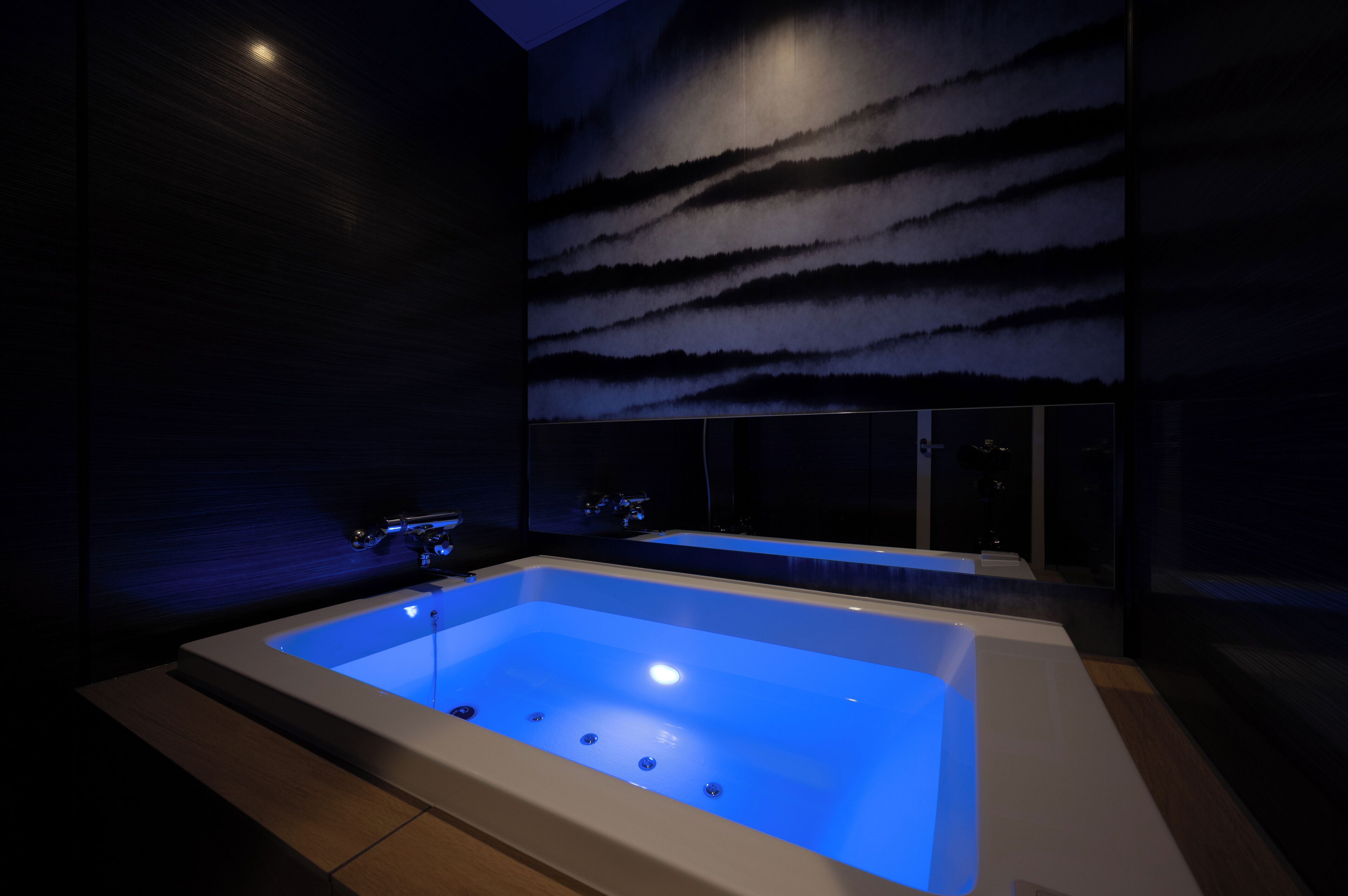 A modern bathroom with a large bathtub, a wall-mounted mirror, and a view of the night sky.