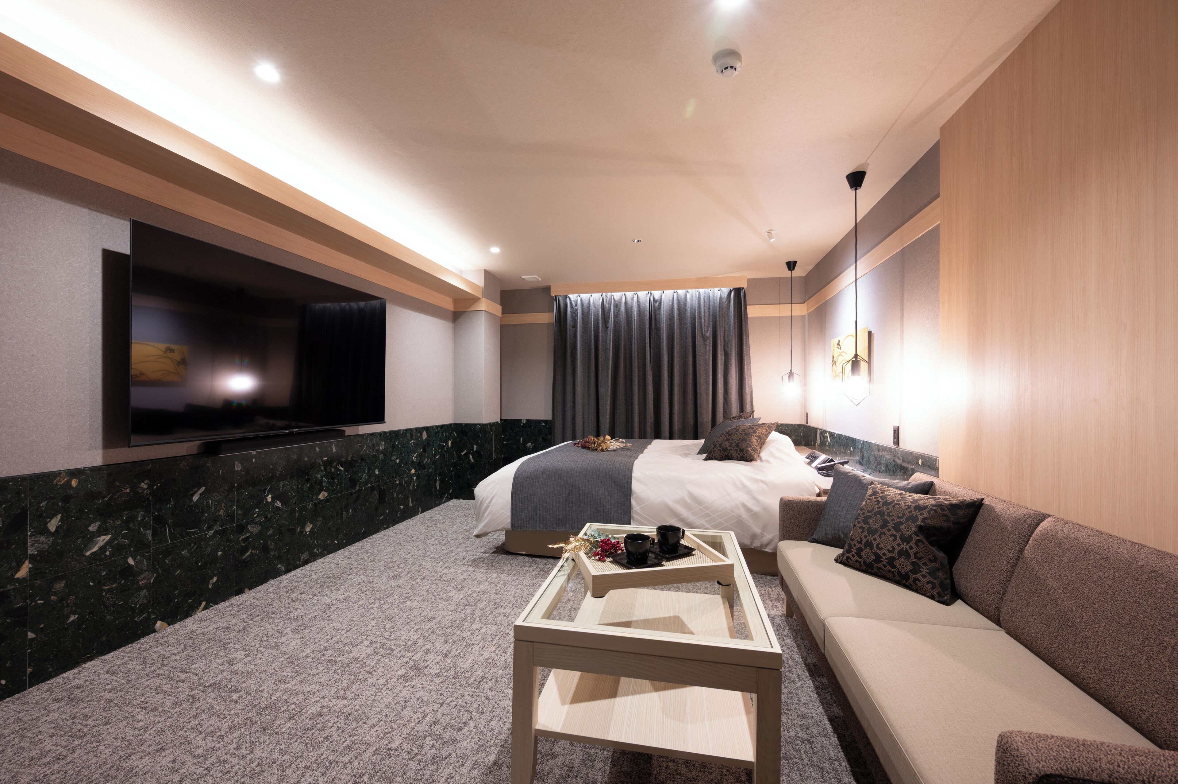 A modern hotel room with a flat-screen TV, a sofa, a bed, and a coffee table.