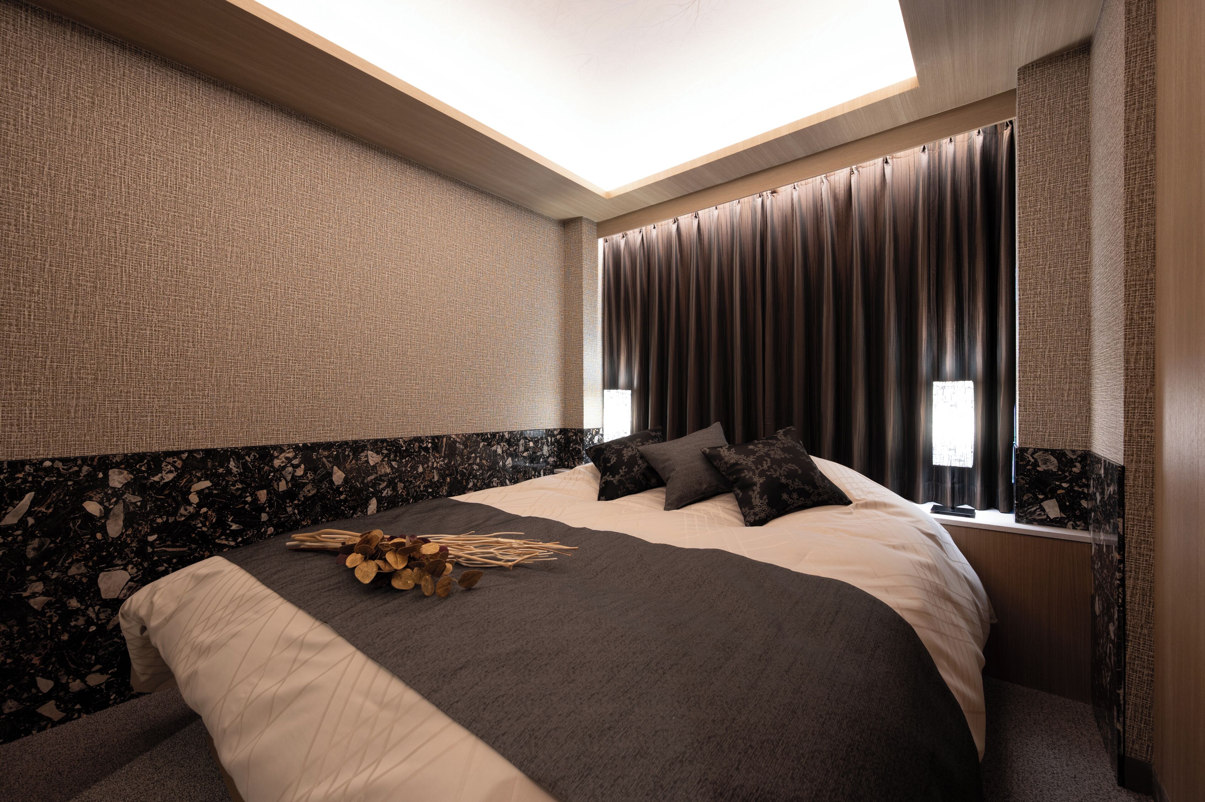 Una camera d'albergo moderna con un letto grande, tende scure e un lucernario.