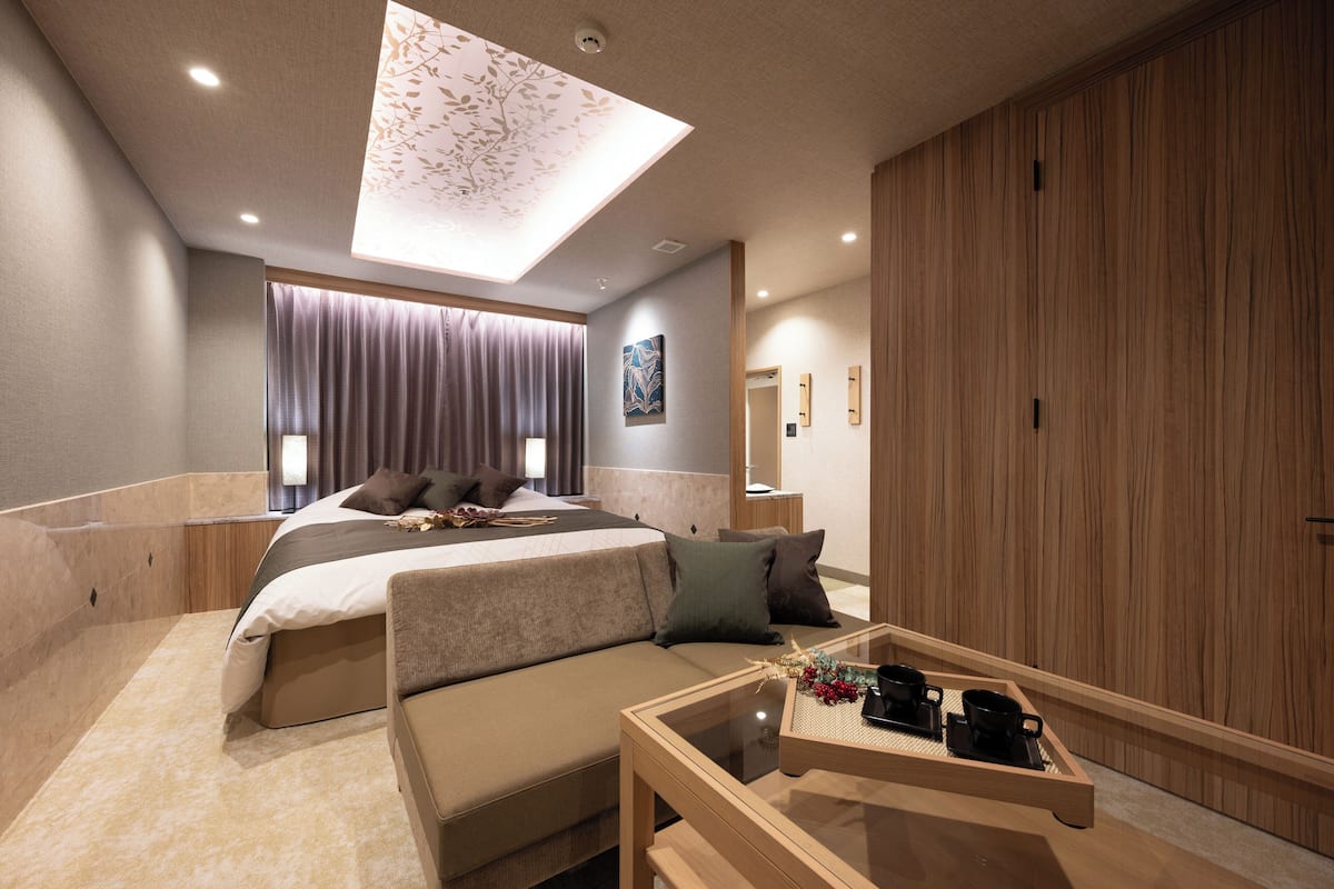 Una habitación de hotel moderna con una cama grande, un sofá, una mesa de centro de cristal y un armario de madera.