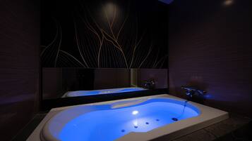 A modern bathroom with a large bathtub, a mirror, and a wall with a leaf pattern.